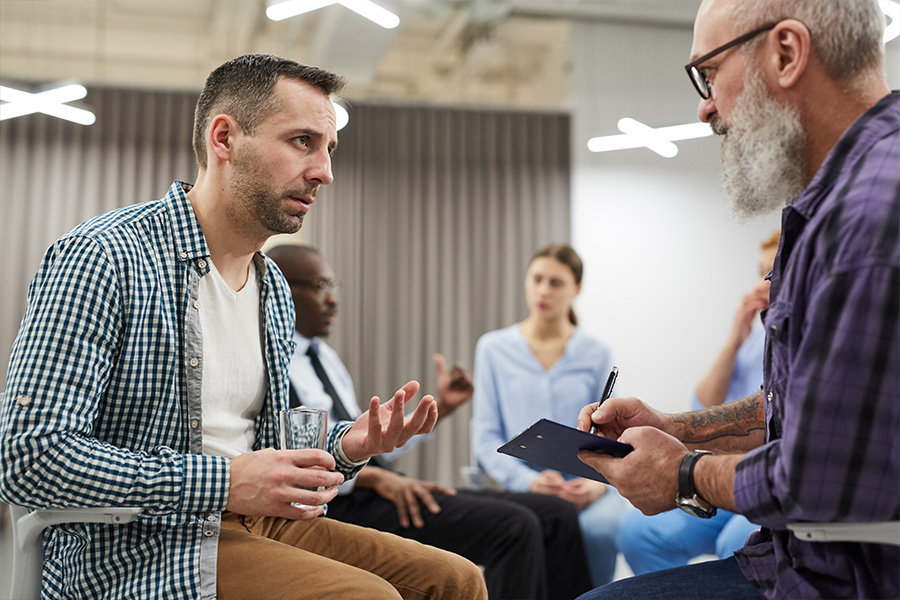 man discussing addiction with therapist in group
