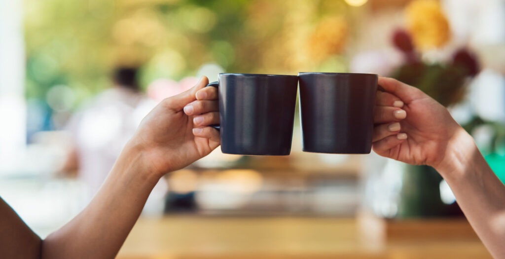 hands of two people touching their mugs together