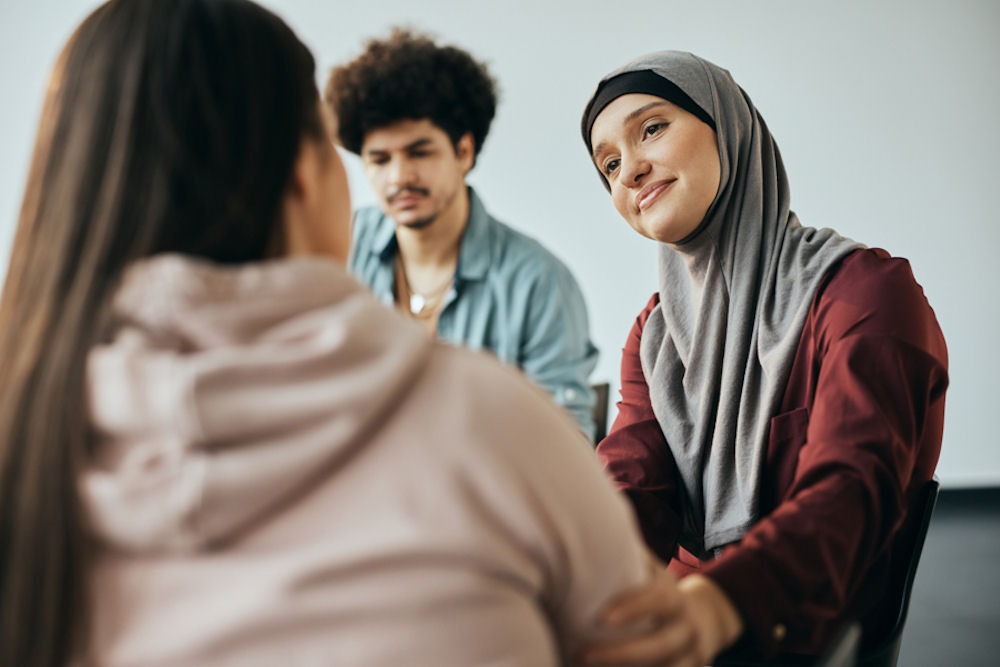 woman in group addiction therapy offering support to another member