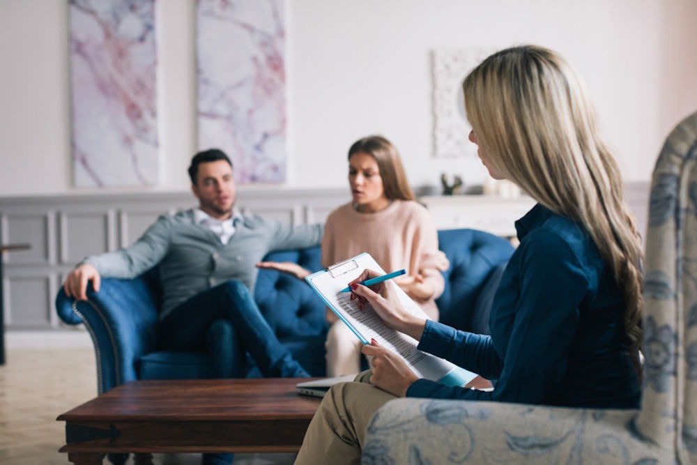 therapist taking notes during couples therapy session as man and woman sit on couch