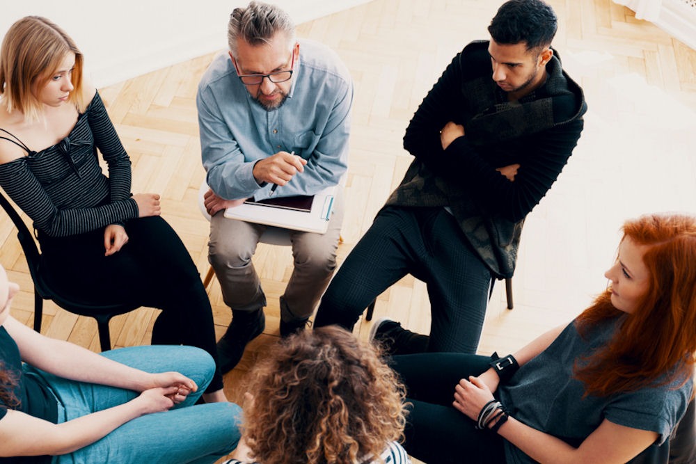 five young adults sitting in circle with therapist for group addiction therapy