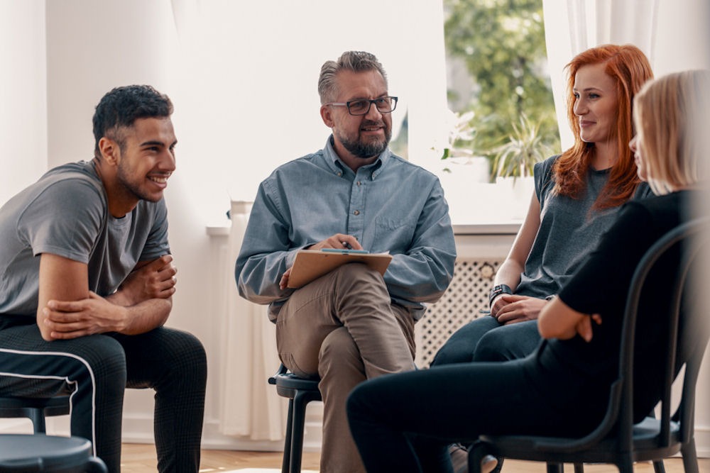 male therapist discussing addiction with small group of men and women in rehab