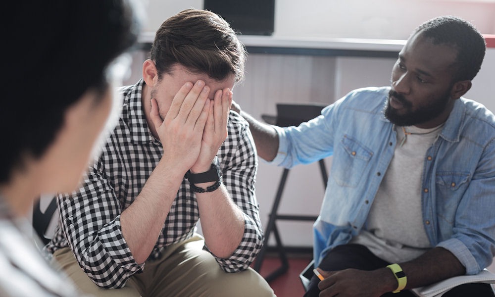 stressed man covering his face while another man places a hand on his shoulder