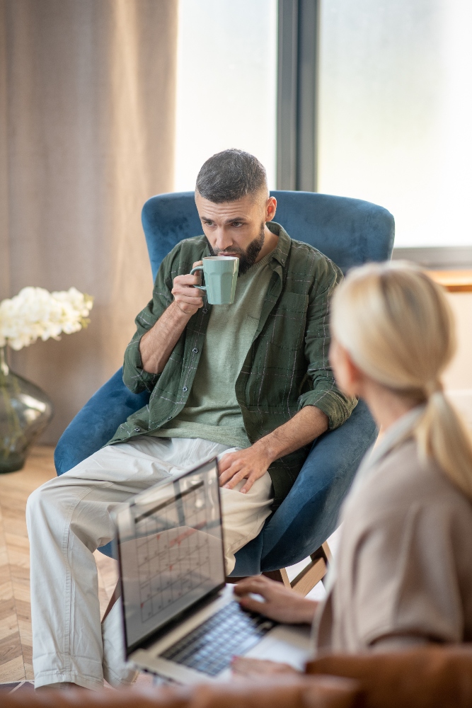 blonde-psychoanalyst-holding-laptop-and-speaking-w-2024-10-11-18-18-17-utc (1) therapist speaking to man with addiction to drugs while working on laptop