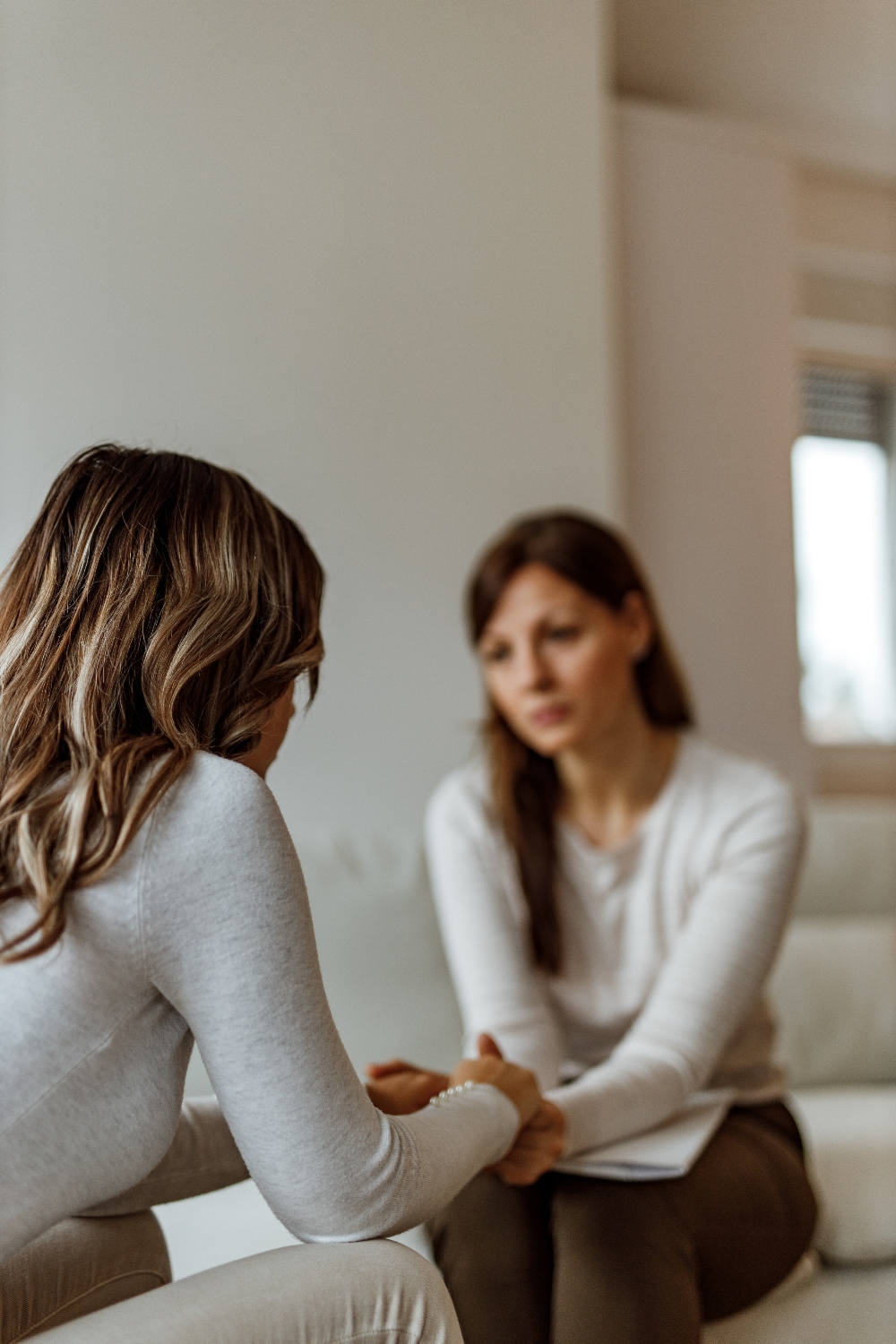 Focus on depressed woman, brunette doctor in the background. young woman speaking with a therapist at a colorado drug rehab facility