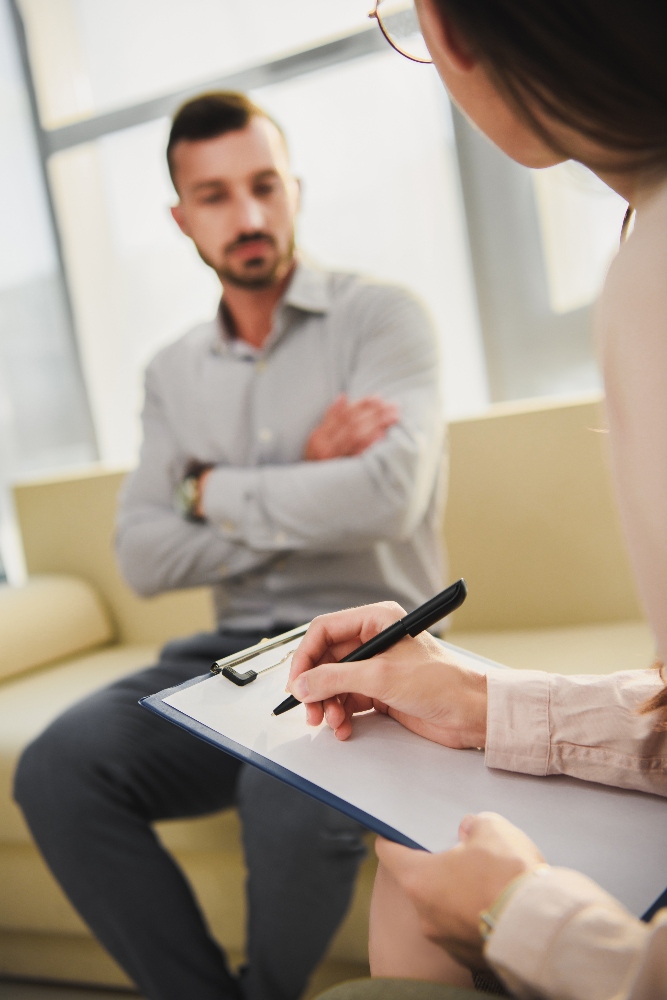 selective focus of patient and psychiatrist writing in clipboard in office man meeting with therapist for php